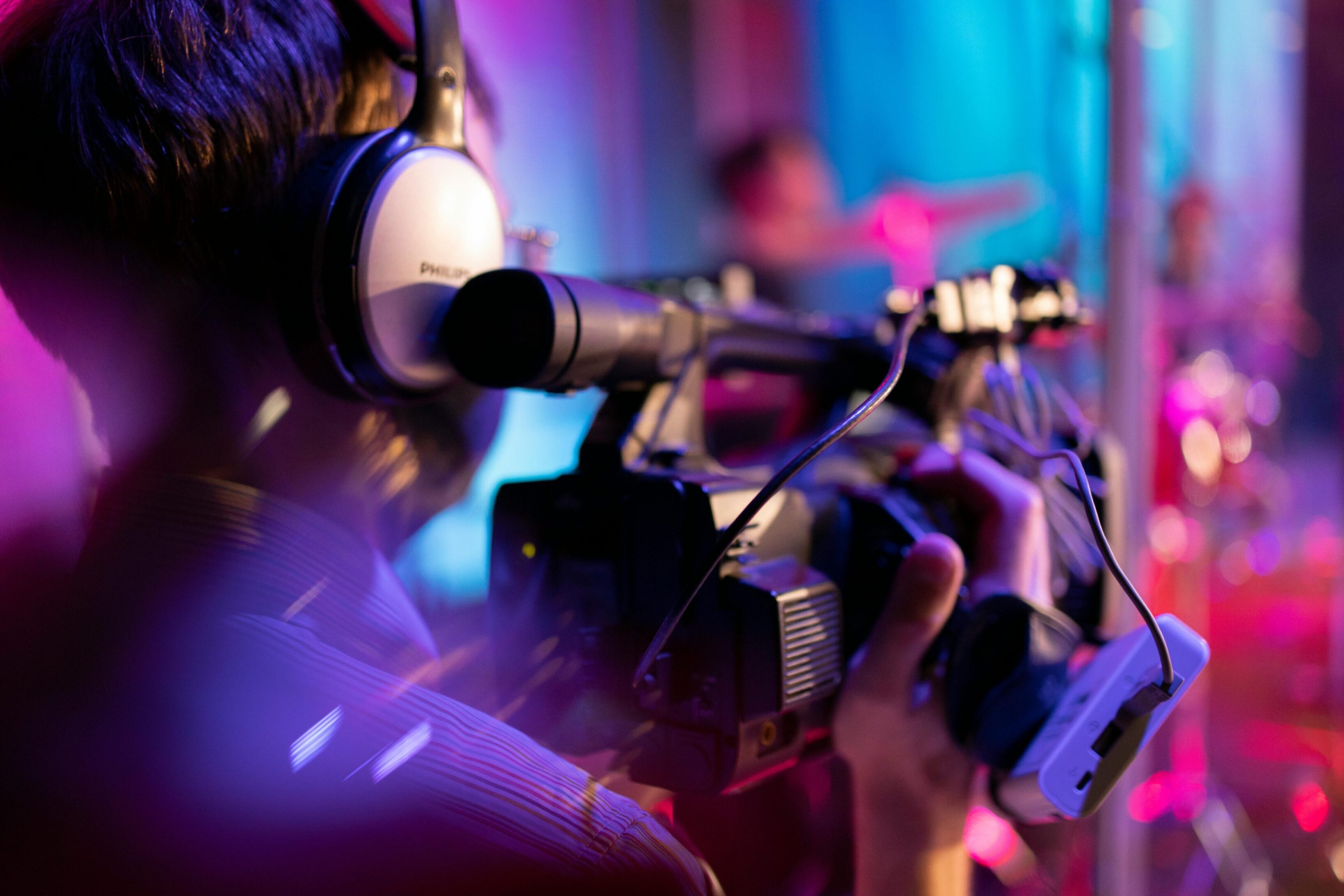 Person filming with a professional video camera in a colorful setting.