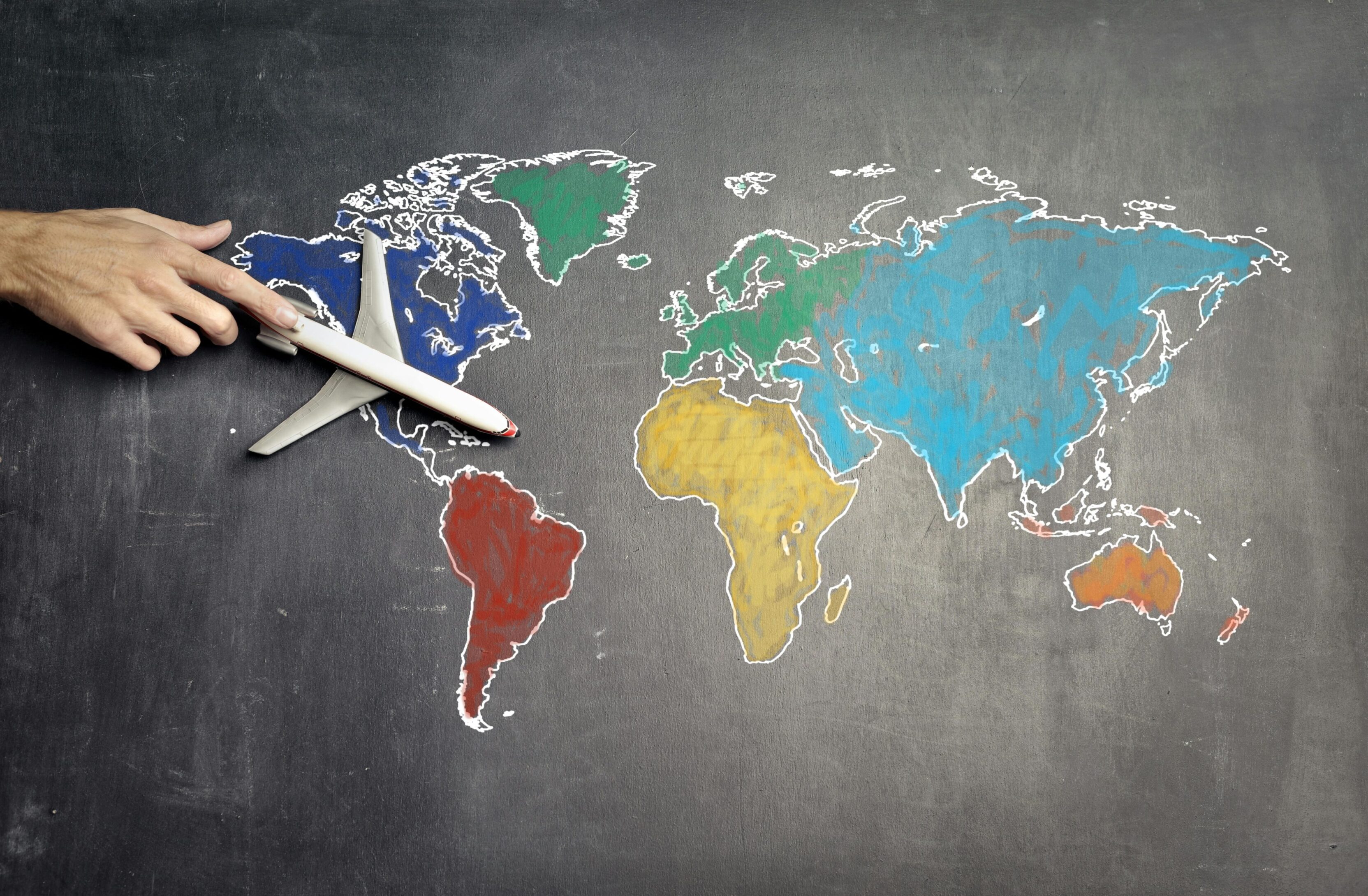 Toy airplane flying over a colorful world map drawn on a chalkboard.